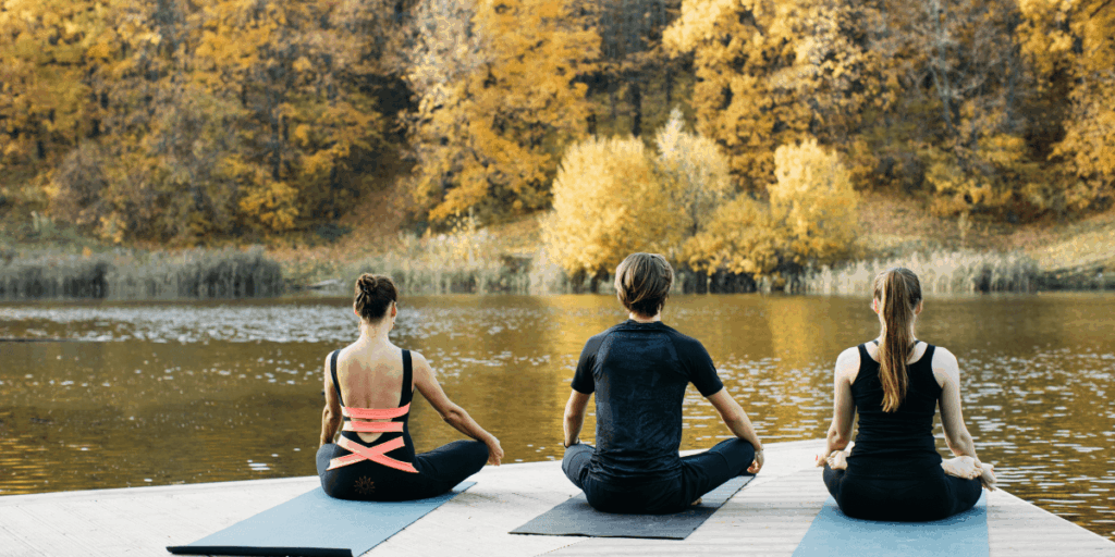 Three individuals practicing yoga on a wooden dock, surrounded by water and greenery, enjoying a peaceful outdoor setting.