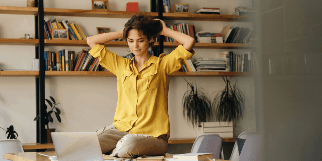 A woman sitting on the floor, head in hands, using her laptop, appears stressed or overwhelmed by her work.