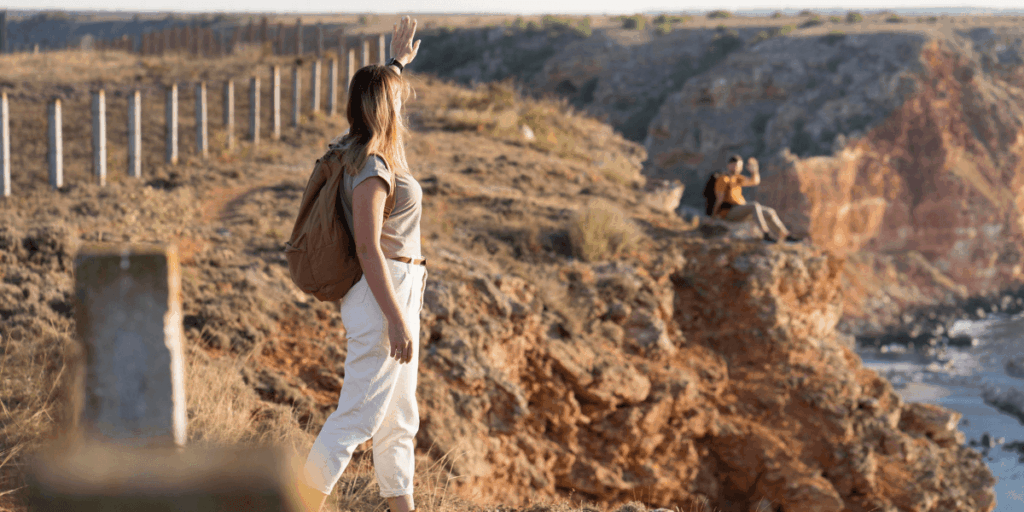 A woman stands on a cliff, gazing out at the vast ocean under a clear blue sky.